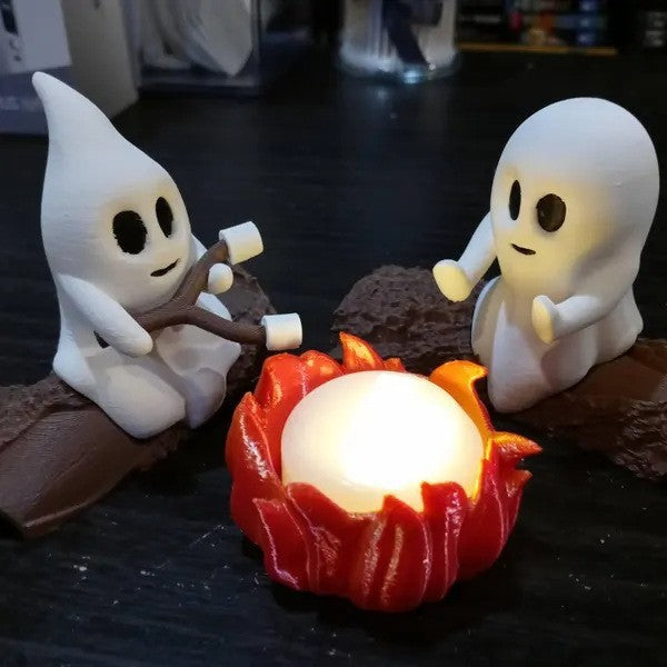 Two ghost figurines around a campfire with marshmallows, on a dark surface.