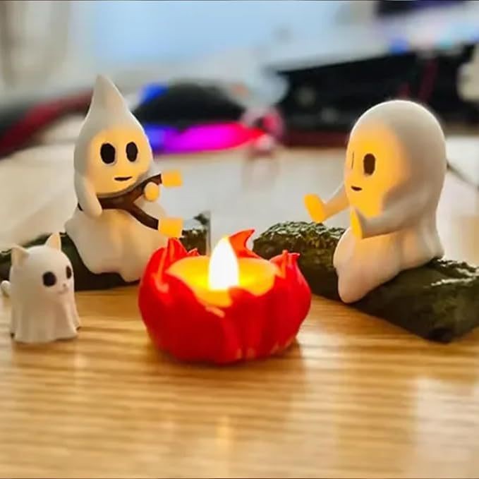 Three small ghost figurines around a lit candle on a wooden surface.