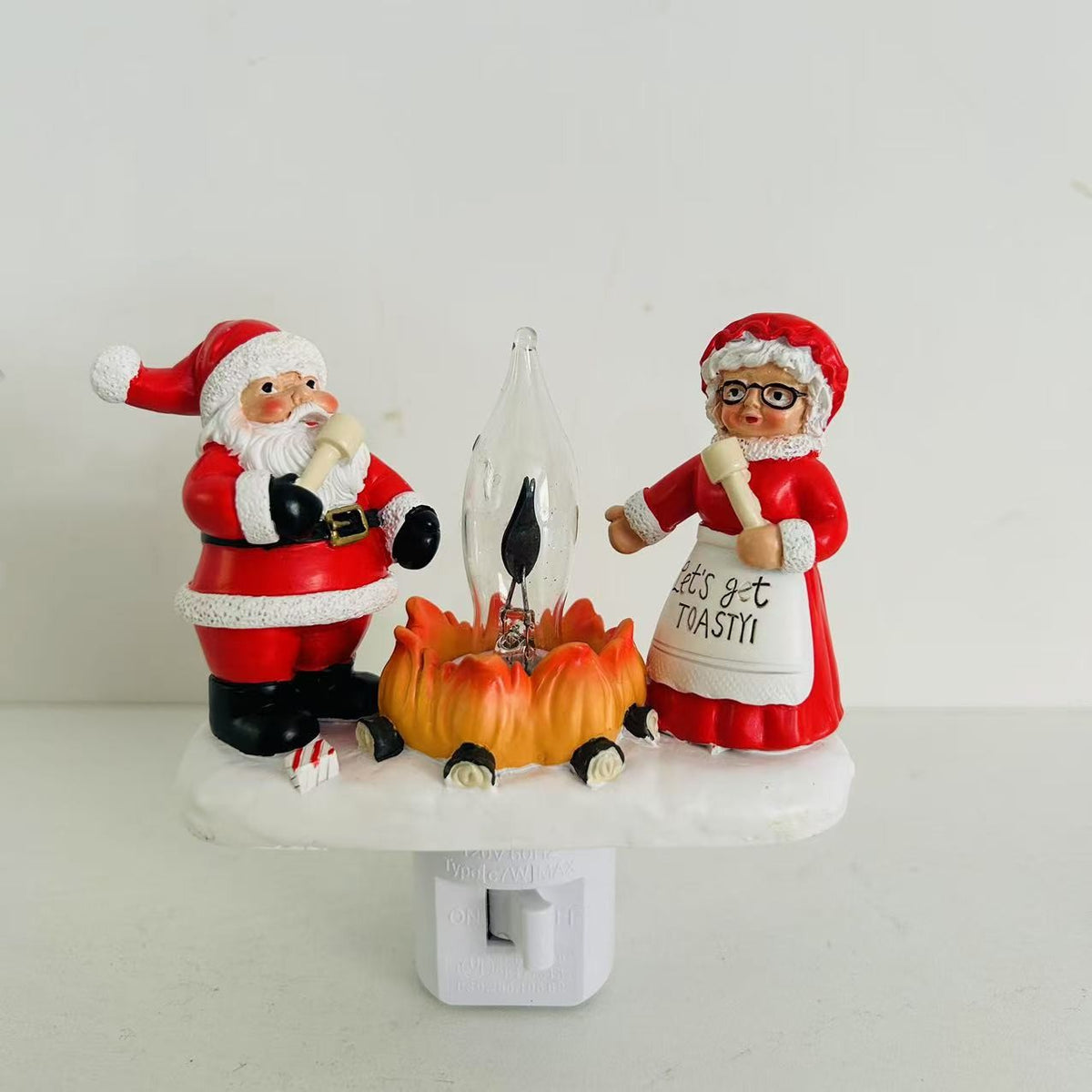 Two Santa Claus figurines by a fire with a white background